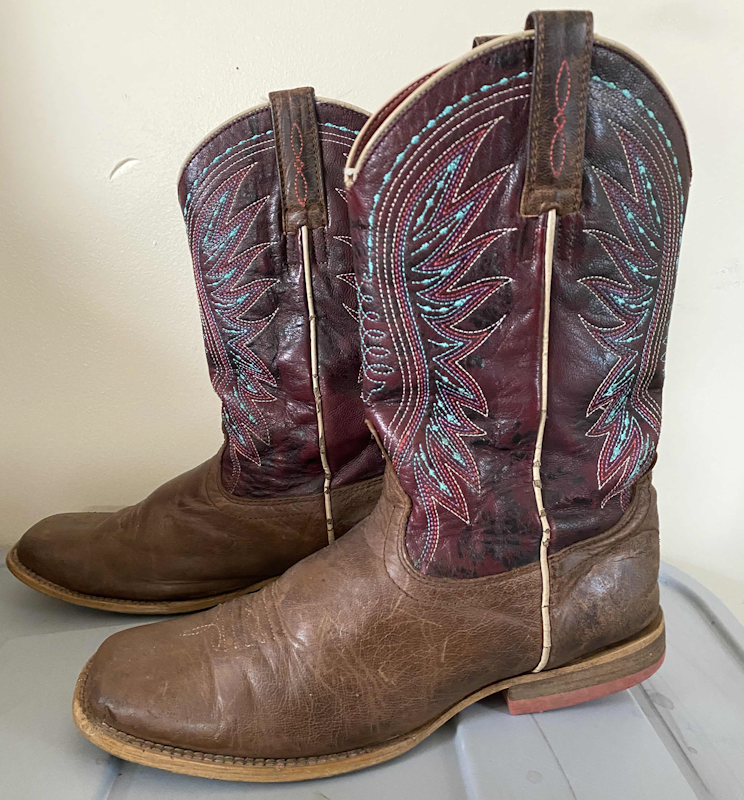 A pair of cowboy boots. They are light brown with a maroon shaft that has red, yellow, and turquoise embroidery.