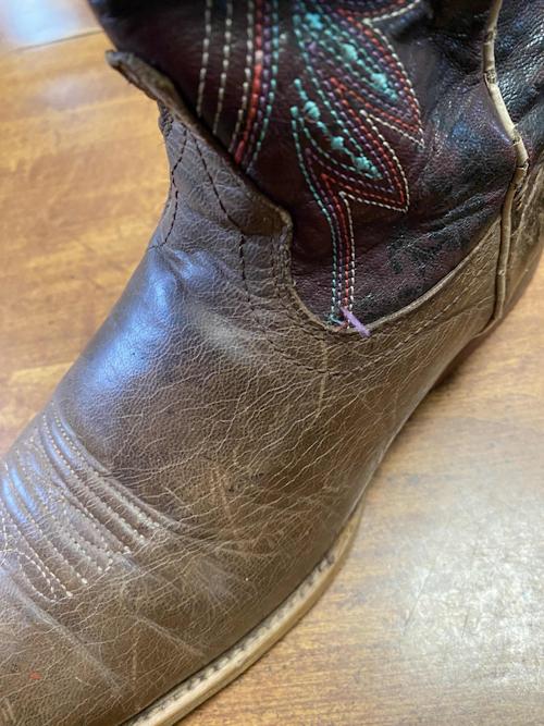 Close-up on the vamp, the brown top part of the boot, showing the dry wrinkled leather and frayed embroidery on the shaft