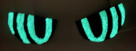 2D Fursuit eyes detached from the head and laying on a surface. It is dark and they are glowing green.