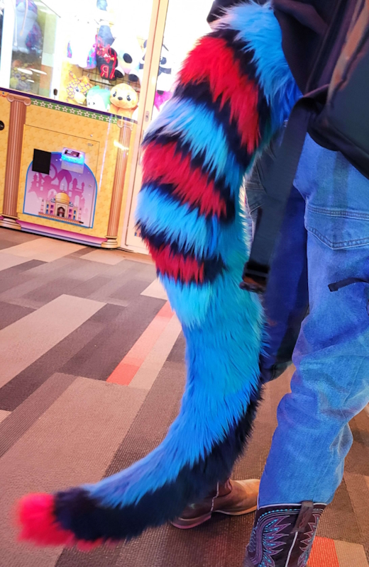 Photograph of a fursuit tail with a green base and red stripes on the top and tail tip.