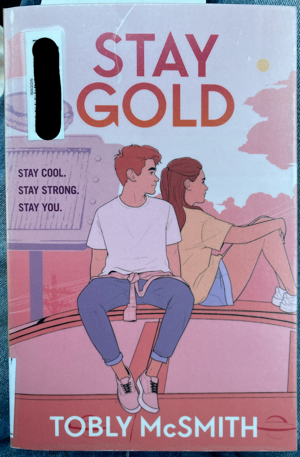 a copy of Stay Gold. the cover is pink toned and depicts a young adult couple sitting on top of a car. the boy is in a white t shirt and jeans, looking towards the girl, who has long brown hair, a loose yellow t shirt, and jean shorts. behind them is the test stay cool stay strong stay you